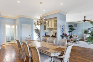 A spacious dining area with a large wooden table and matching chairs, a chandelier, and a staircase leading to a kitchen. - Permuda Private Island by Topsail Realty (Sneads Ferry)