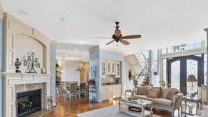 A spacious living room with hardwood floors, a fireplace, a ceiling fan, and a large window providing natural light. - Permuda Private Island by Topsail Realty (Sneads Ferry)