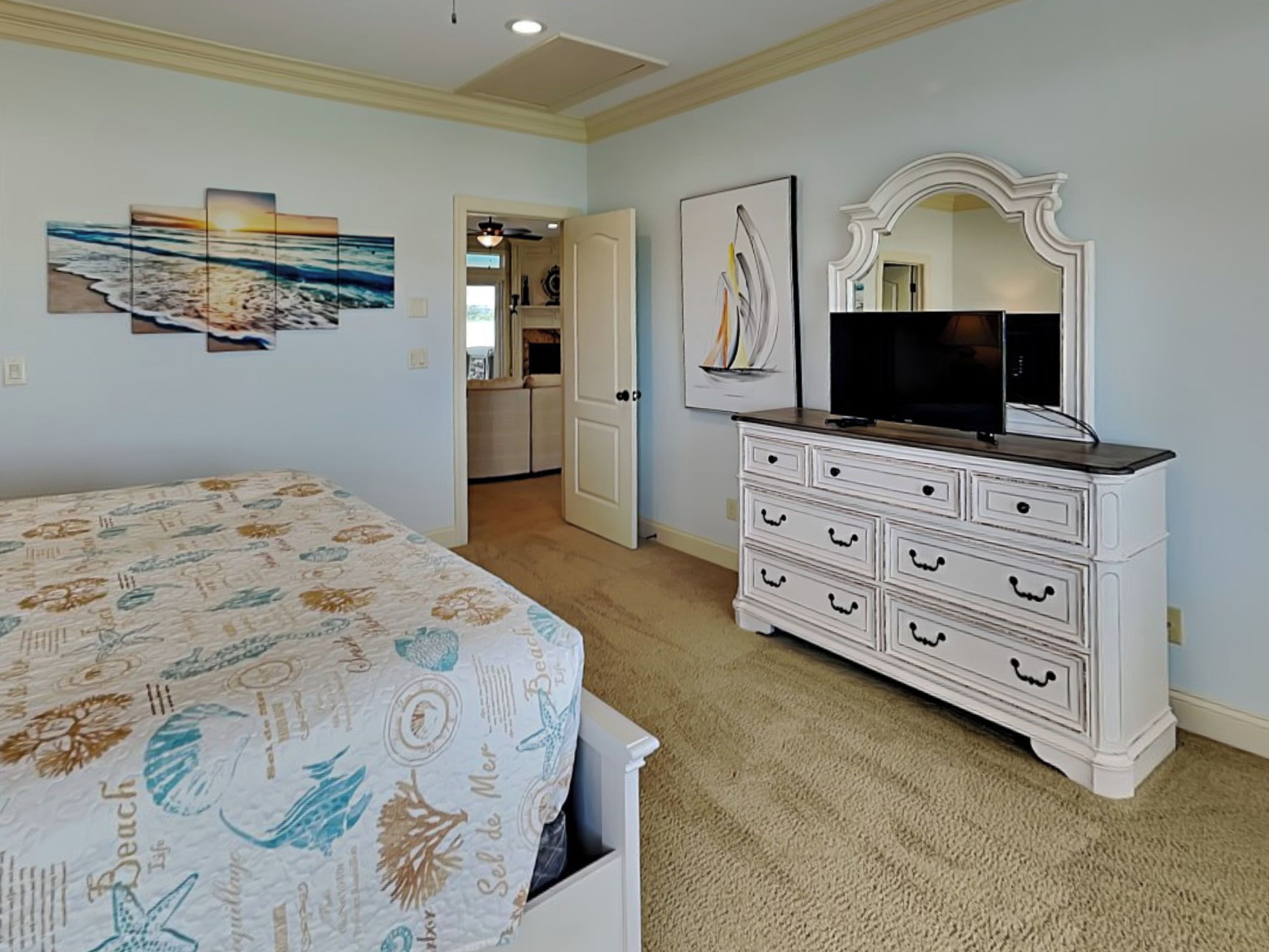 A bedroom with a bed, dresser, TV, and artwork on the wall.