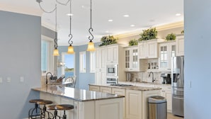 A modern kitchen with white cabinets, stainless steel appliances, and a central island with bar stools. - Permuda Private Island by Topsail Realty (Sneads Ferry)