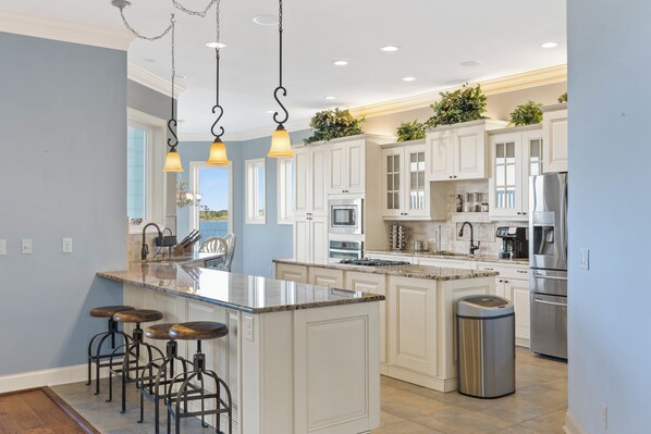 A modern kitchen with white cabinets, stainless steel appliances, and a central island with bar stools. - Permuda Private Island by Topsail Realty (Sneads Ferry)