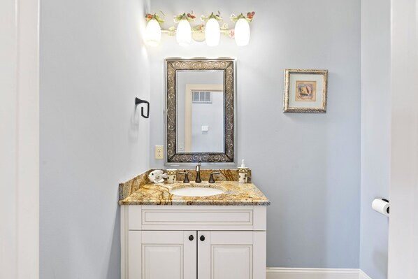 A bathroom with a marble sink, white cabinets, a large mirror with a decorative frame, and a small framed picture on the wall.
