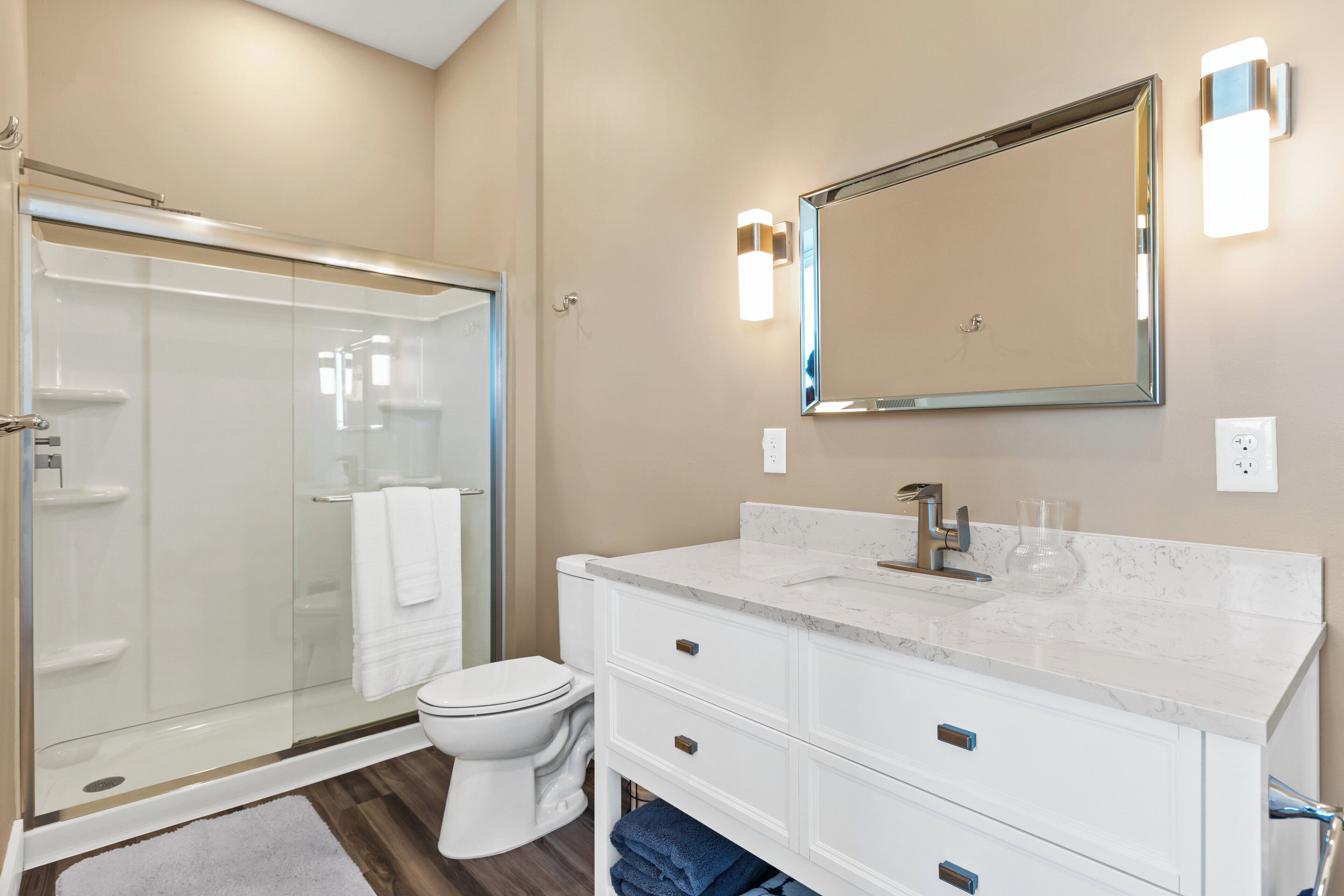 A modern bathroom with a glass shower enclosure, a white toilet, a marble sink vanity, and a large mirror.