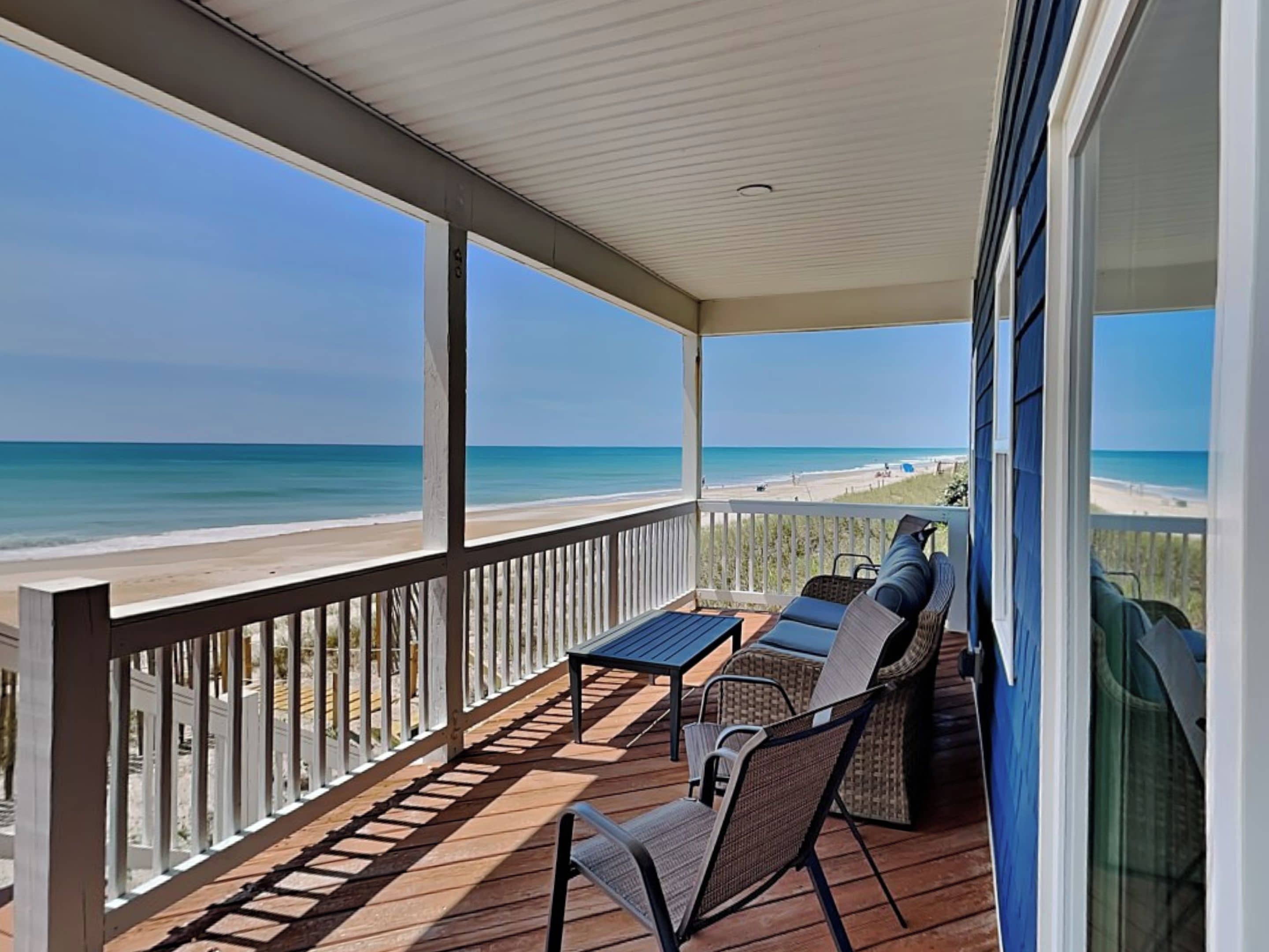 A covered deck with a view of the beach, featuring a table and two chairs.