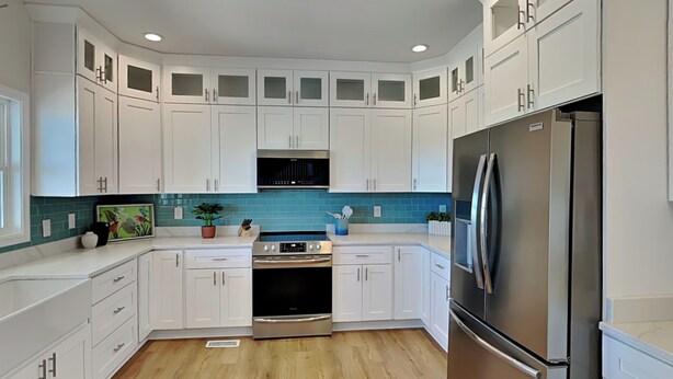 A modern kitchen with white cabinets, a stainless steel refrigerator, and a blue backsplash. - Pelican Landing by Topsail Realty (Sneads Ferry)