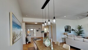 A spacious living area with a wooden dining table, white sofas, and hanging pendant lights. - Pelican Landing by Topsail Realty (Sneads Ferry)