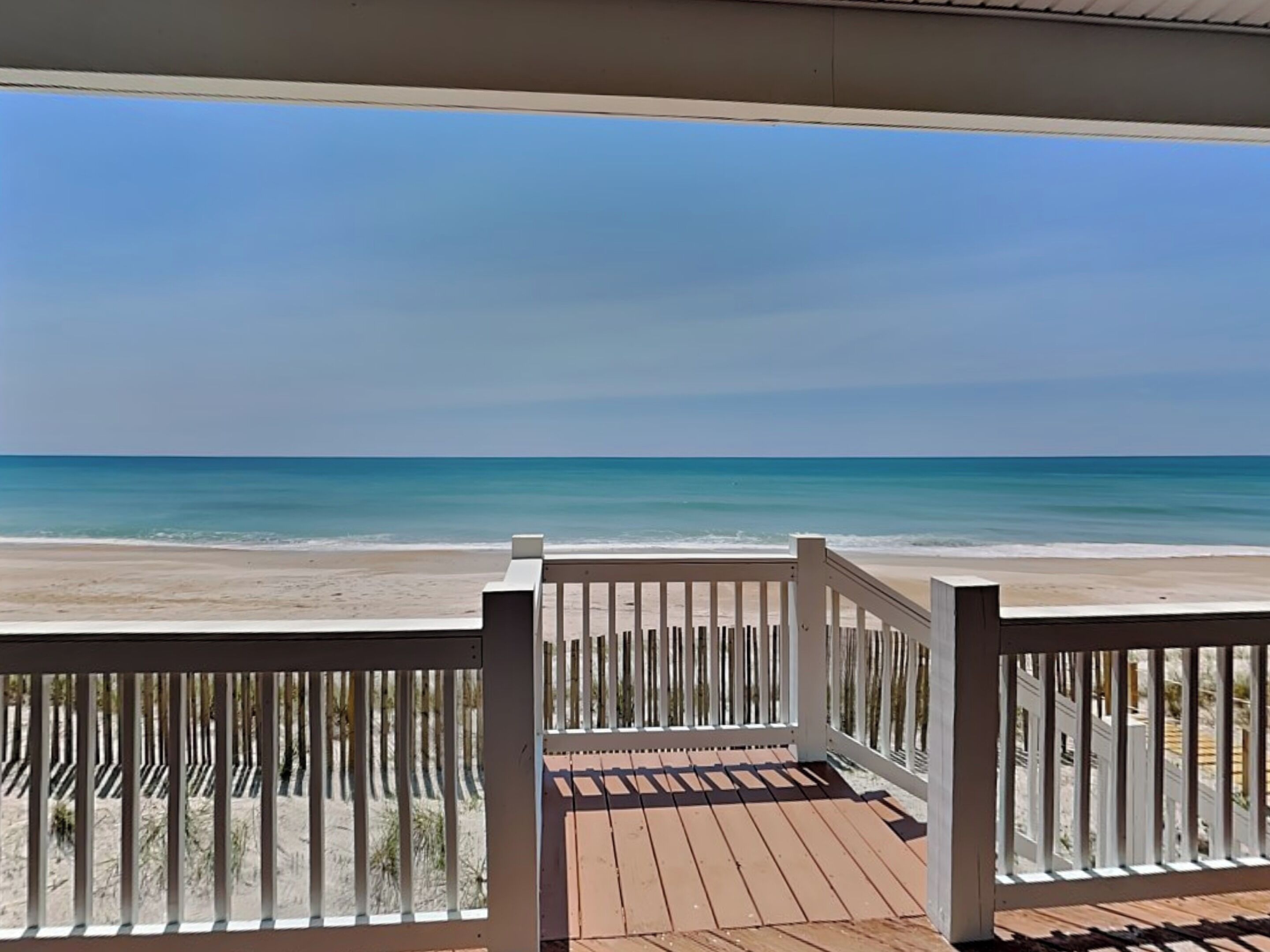 Une terrasse en bois avec des rampes blanches donnant sur une plage.