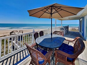 A covered outdoor seating area with wicker furniture and a table, overlooking a beach.