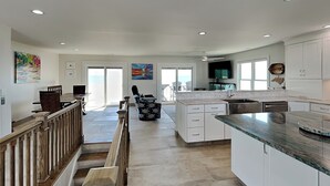 Una cocina amplia con armarios blancos, una isla grande y un comedor con barandal de madera.