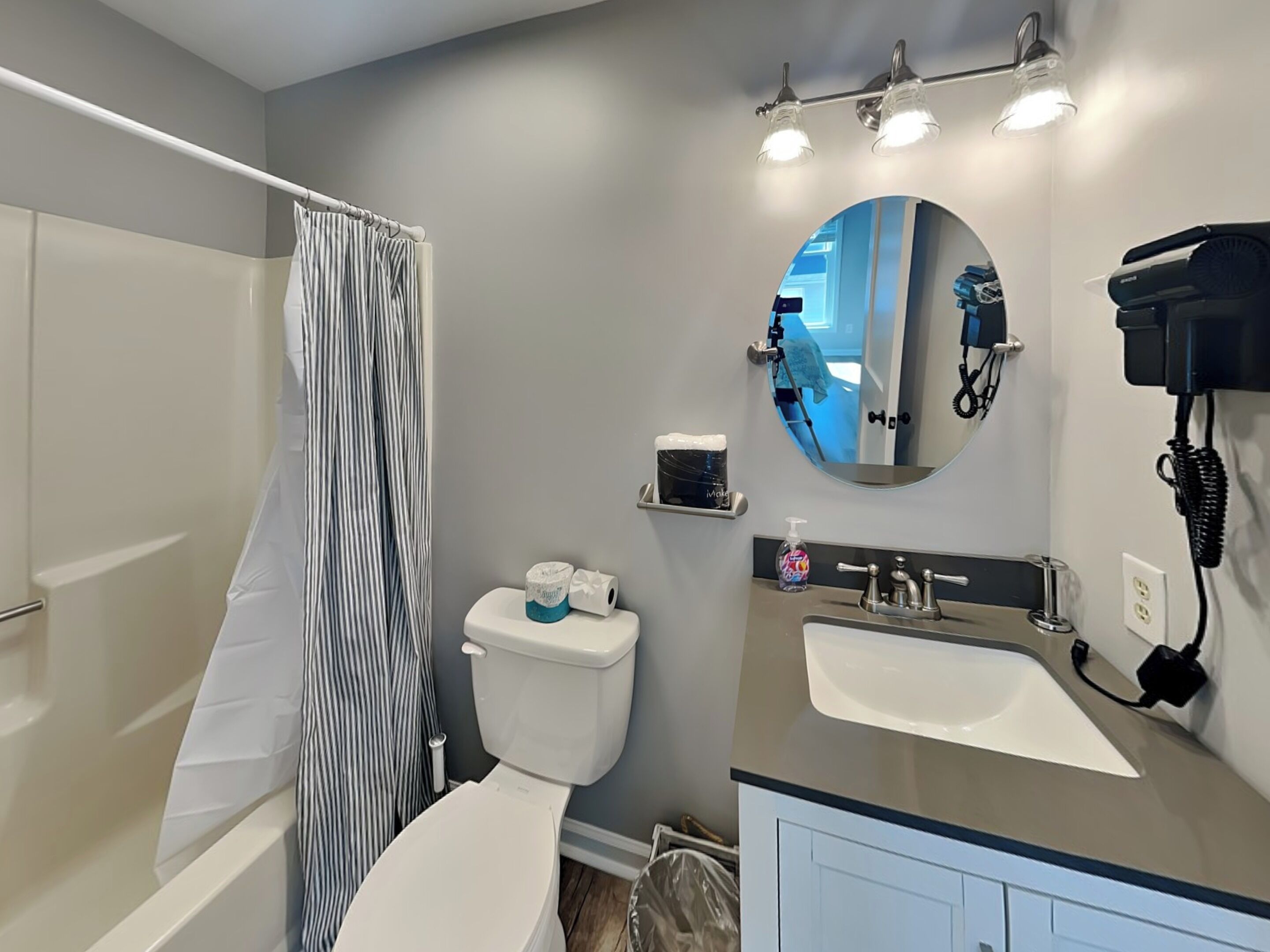 A bathroom with a shower, toilet, sink, and a mirror with a phone.
