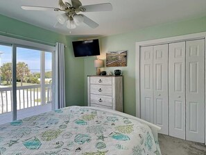 A bedroom with a bed, a ceiling fan, a TV, a dresser, and a door. - Salty Seahorse by Topsail Realty (Sneads Ferry)