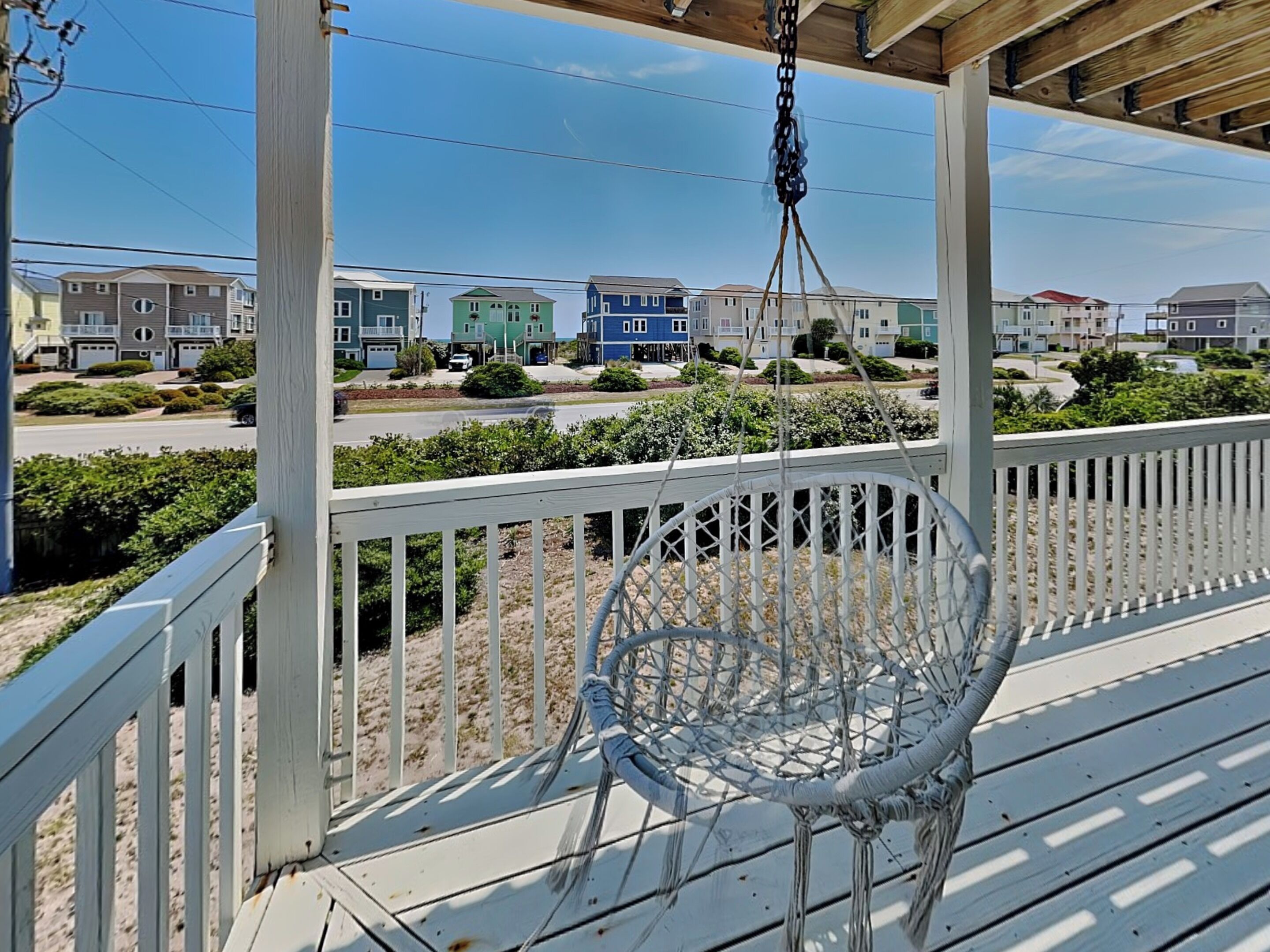 A porch with a swing chair, wooden railings, and a view of a residential area with houses.