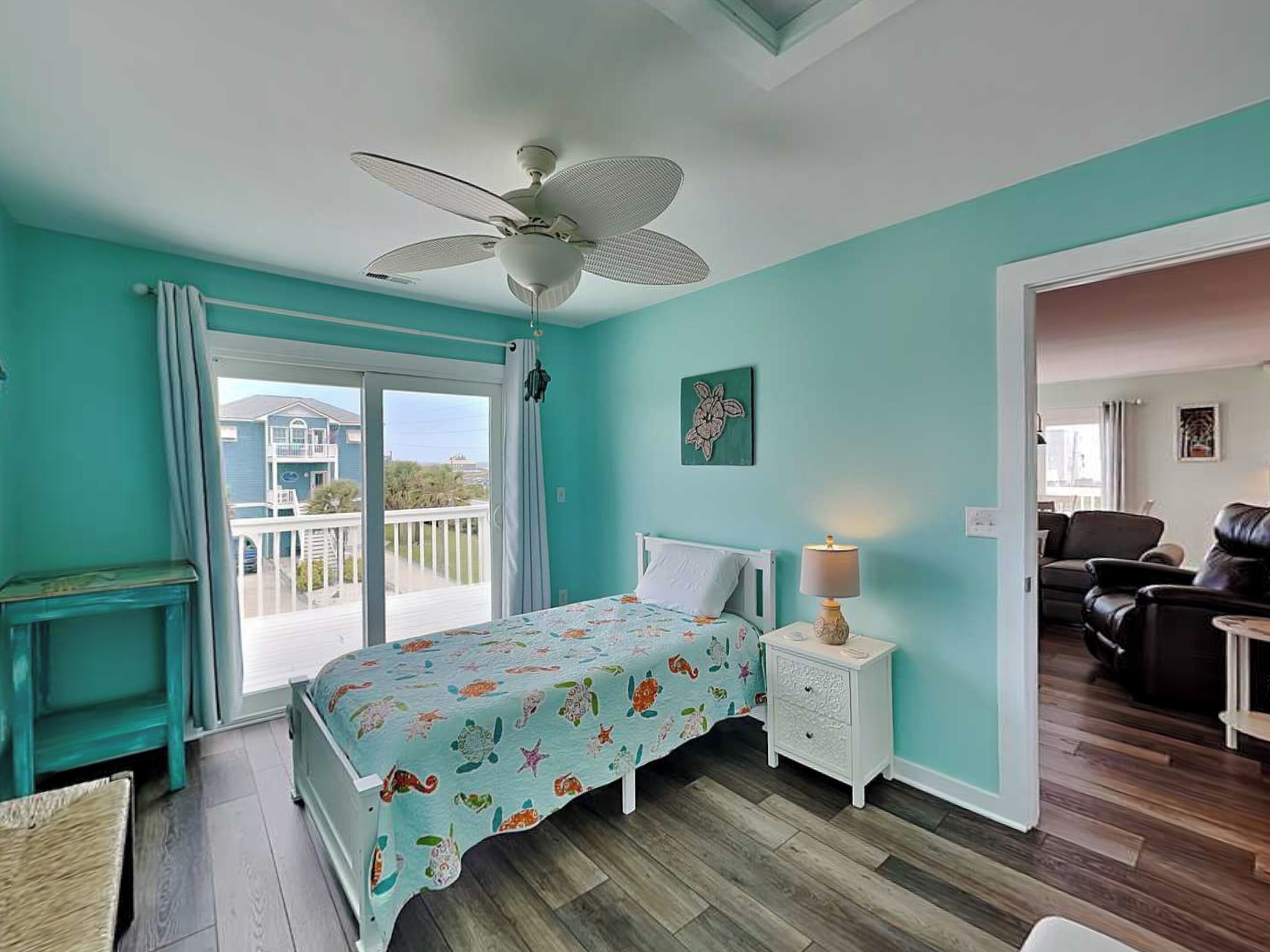 A bedroom with a bed, a nightstand, a ceiling fan, a window with curtains, and a view of a balcony.