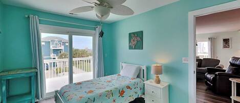 A bedroom with a bed, a nightstand, a ceiling fan, a window with curtains, and a view of a balcony.