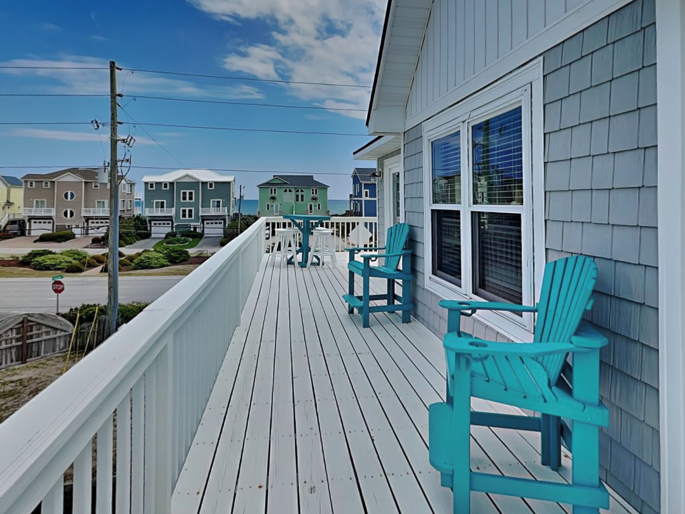 A wooden deck with turquoise Adirondack chairs, a railing, and a view of houses in the background.
