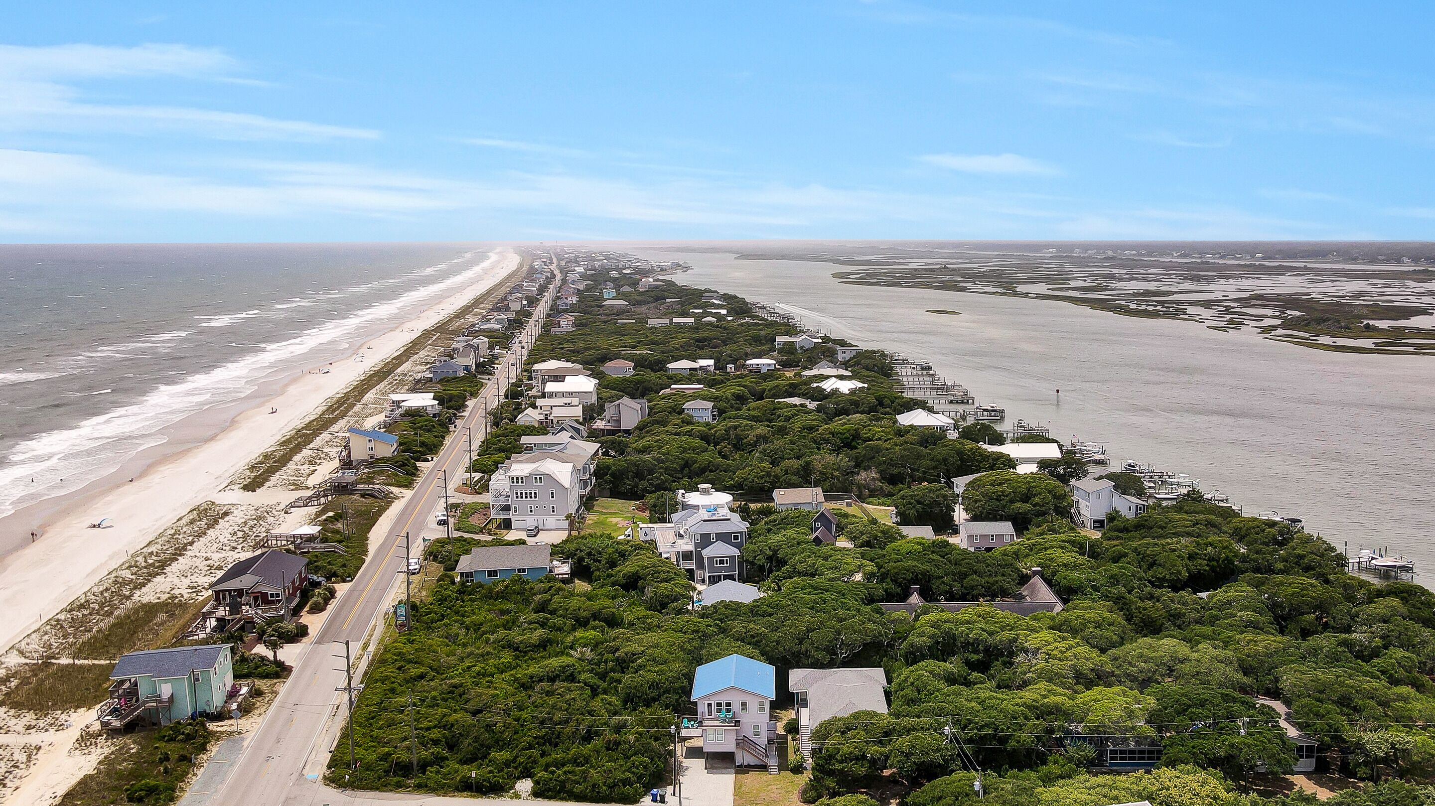 Une zone résidentielle côtière avec des maisons le long de la plage, un ciel dégagé et une vue sur l’océan.