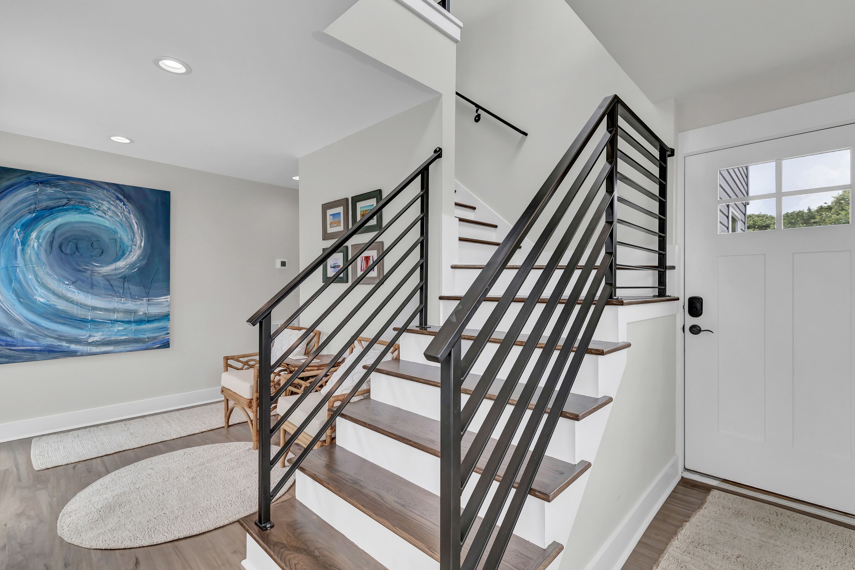 A modern staircase with black railings, a white door with a window, and a large abstract painting on the wall.