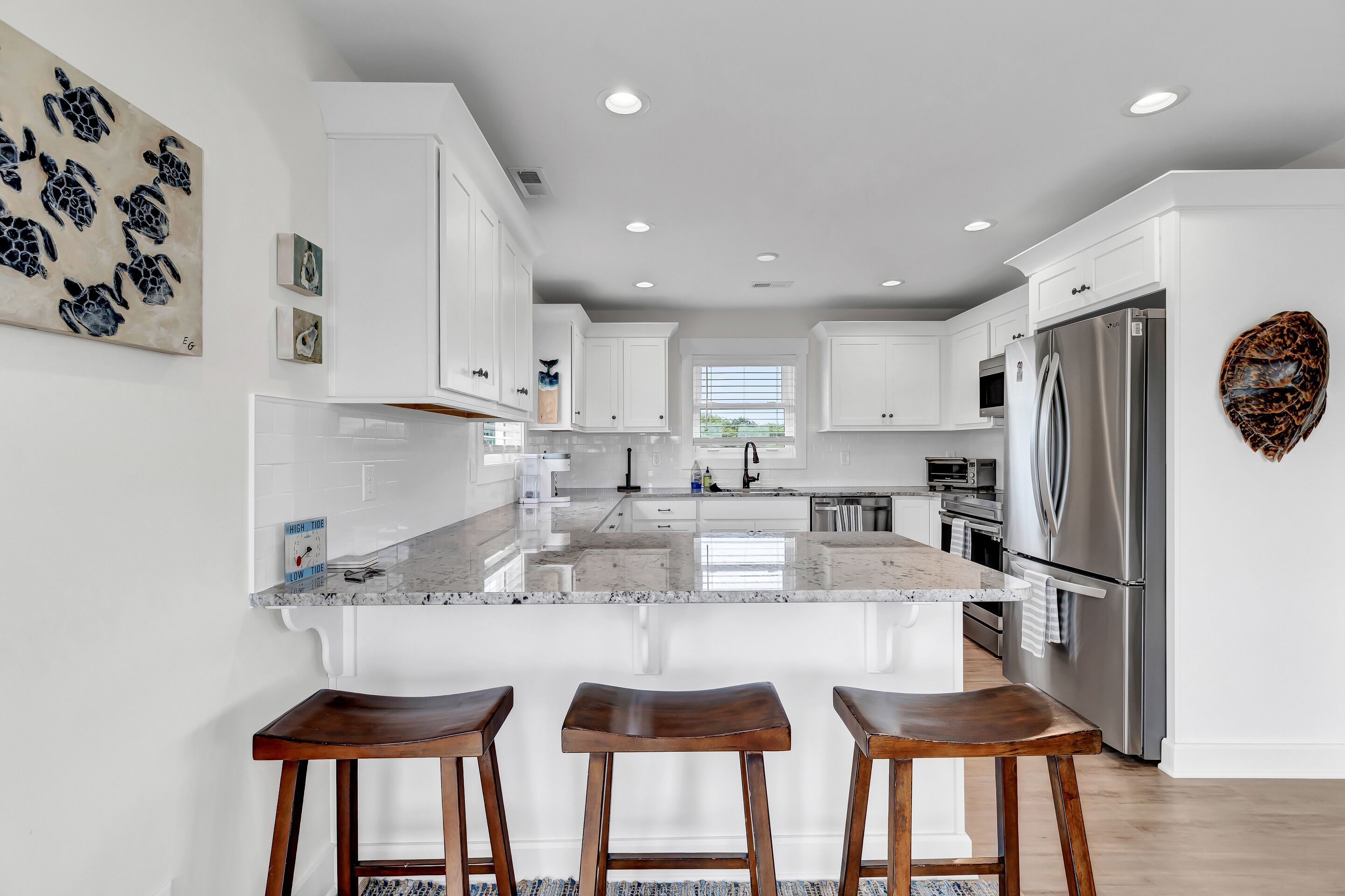 A modern kitchen with white cabinetry, a large island with stools, stainless steel appliances, and artwork on the walls.