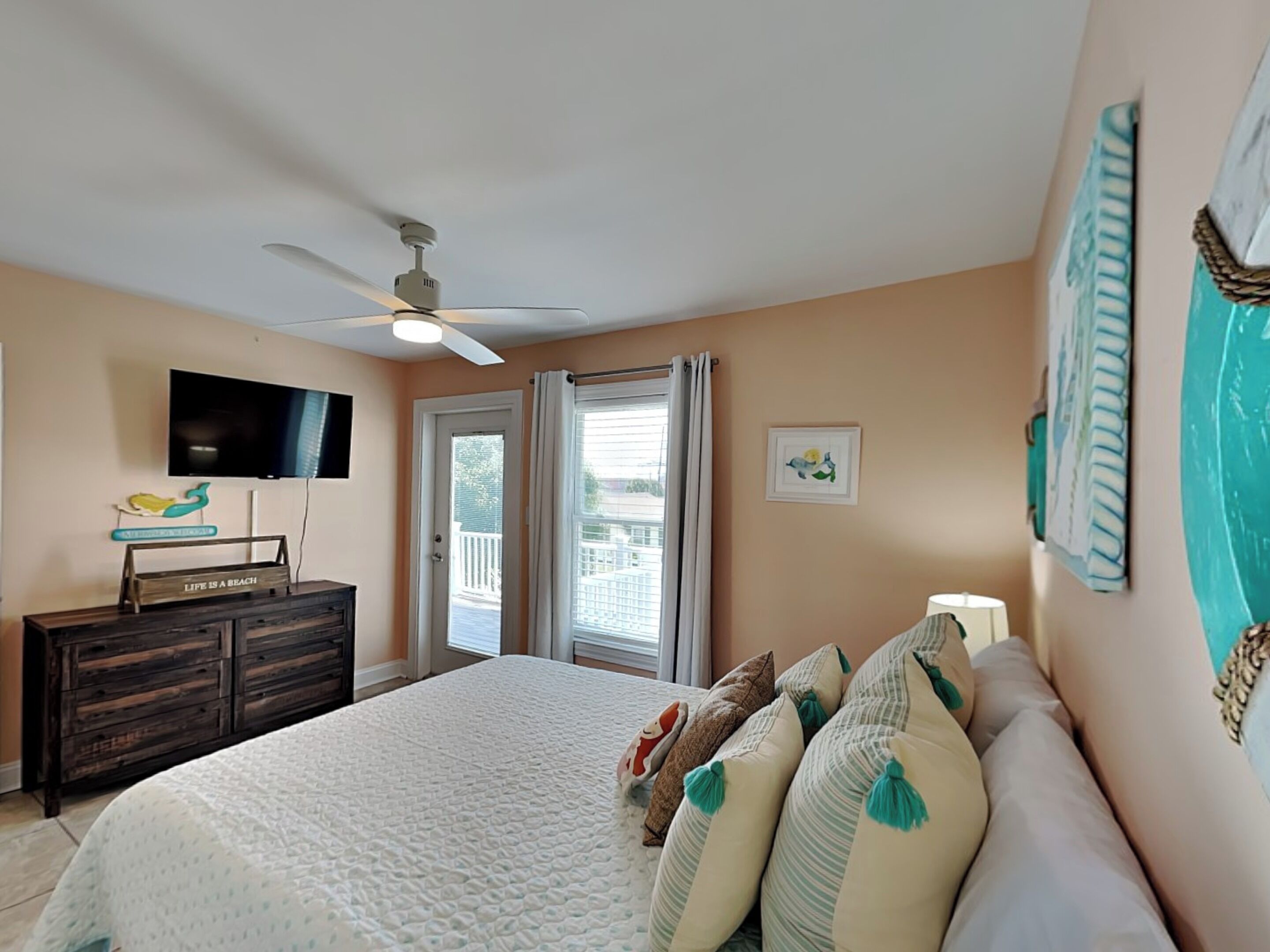 A bedroom with a bed, a ceiling fan, a TV, a dresser, and a balcony door.