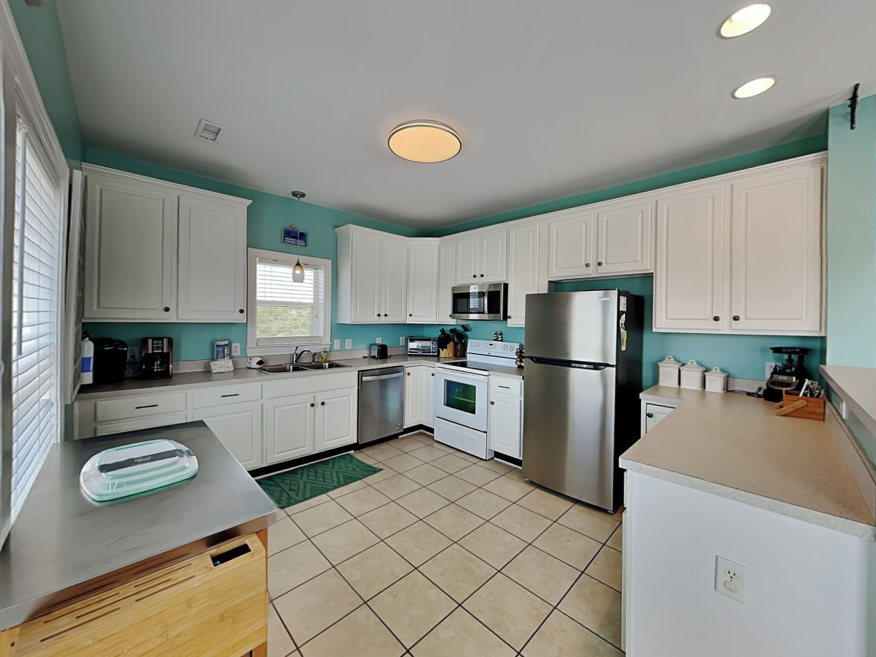 A modern kitchen with white cabinets, stainless steel appliances, and a teal accent wall.