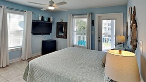 Une chambre à coucher comprenant un lit, un ventilateur de plafond, une télévision, une commode et une fenêtre avec des rideaux.