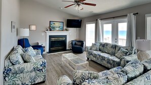 A living room with a fireplace, a ceiling fan, a television, and a view of the ocean. - Renegade by Topsail Realty (Holly Ridge)