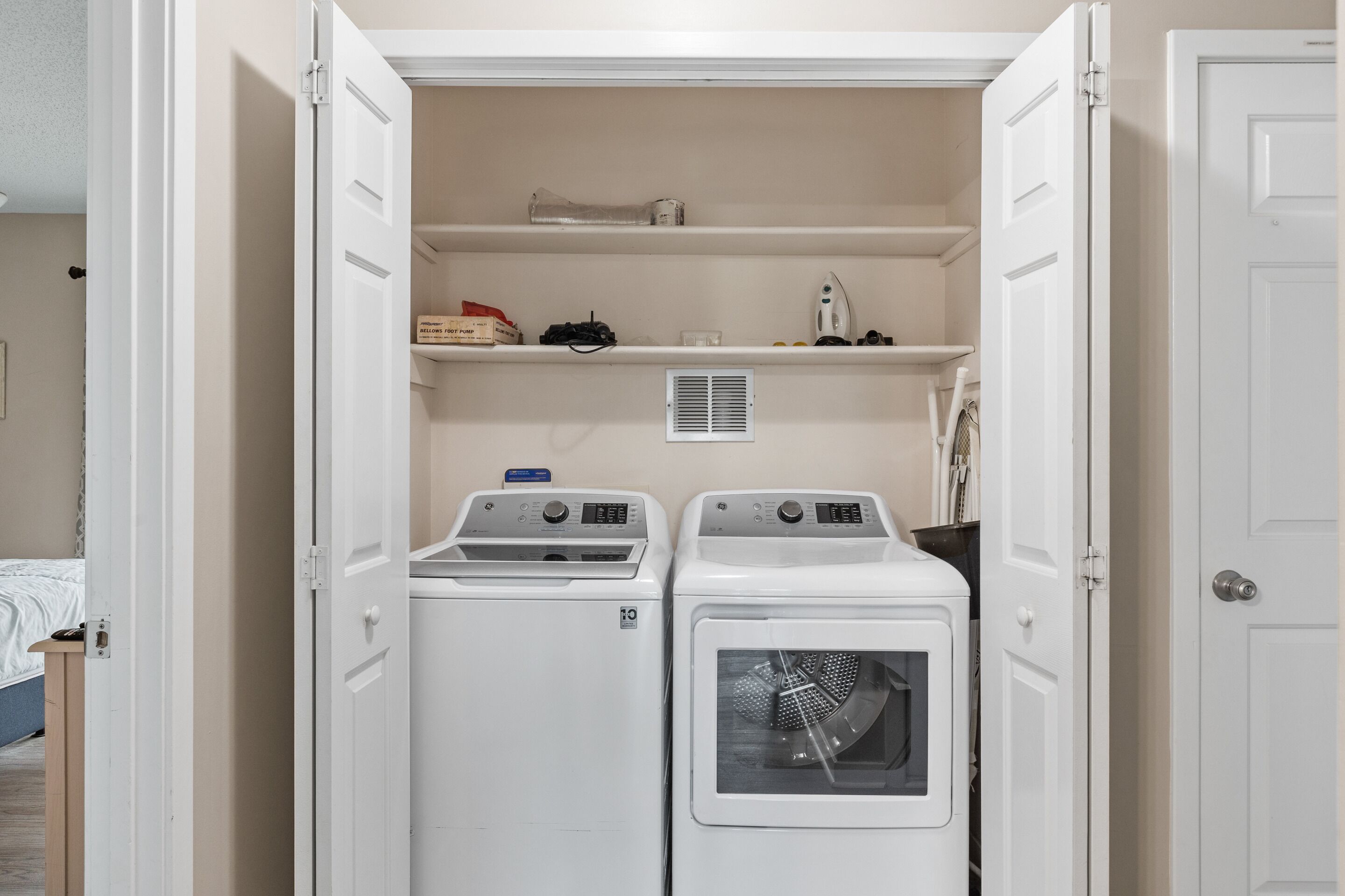 Une buanderie équipée de deux machines à laver et deux sèche-linge superposés, d’une étagère contenant des produits de lessive et d’une bouche d’aération au mur.