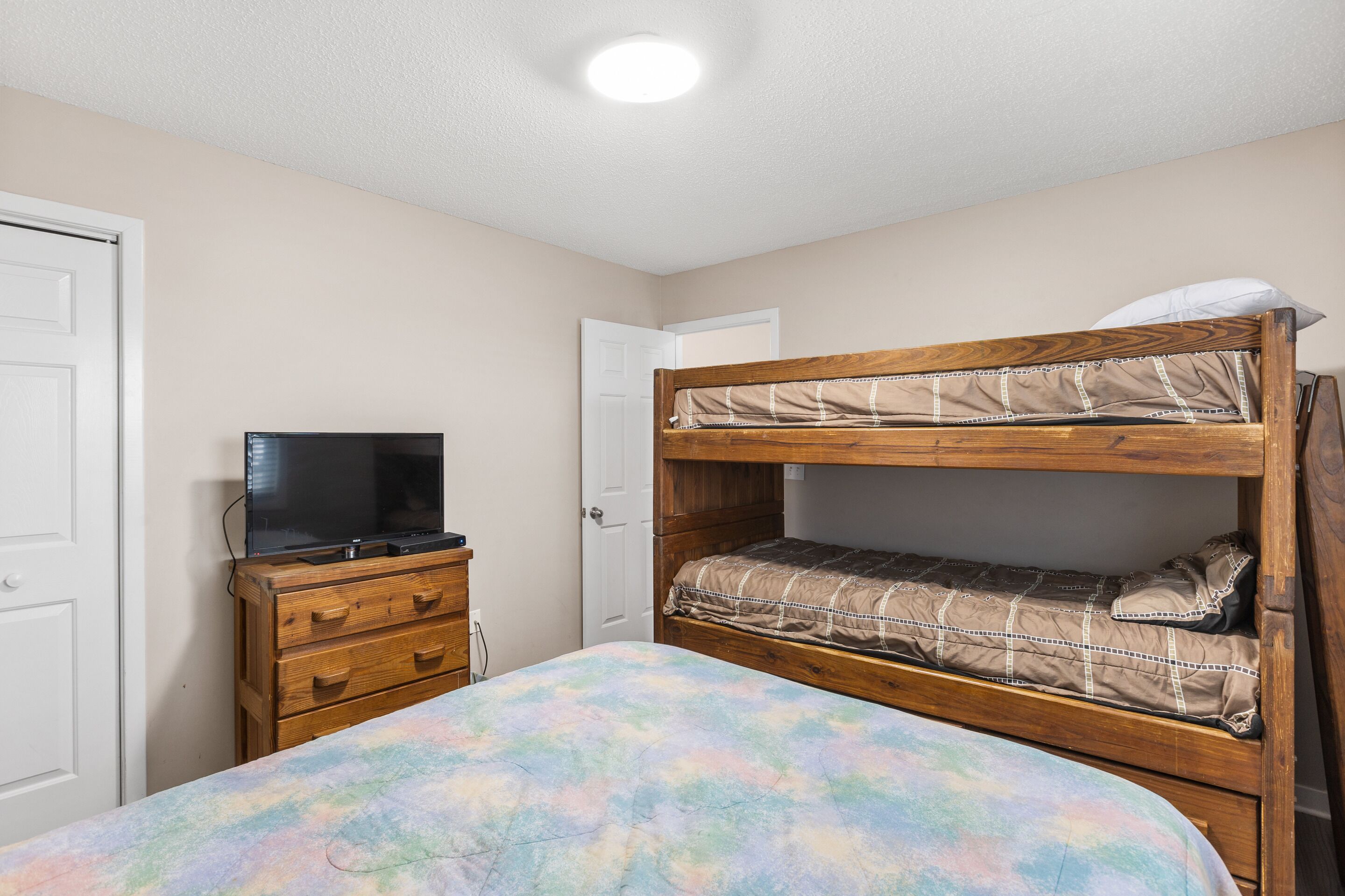 A bunk bed with a television on a dresser, a door, and a ceiling light.