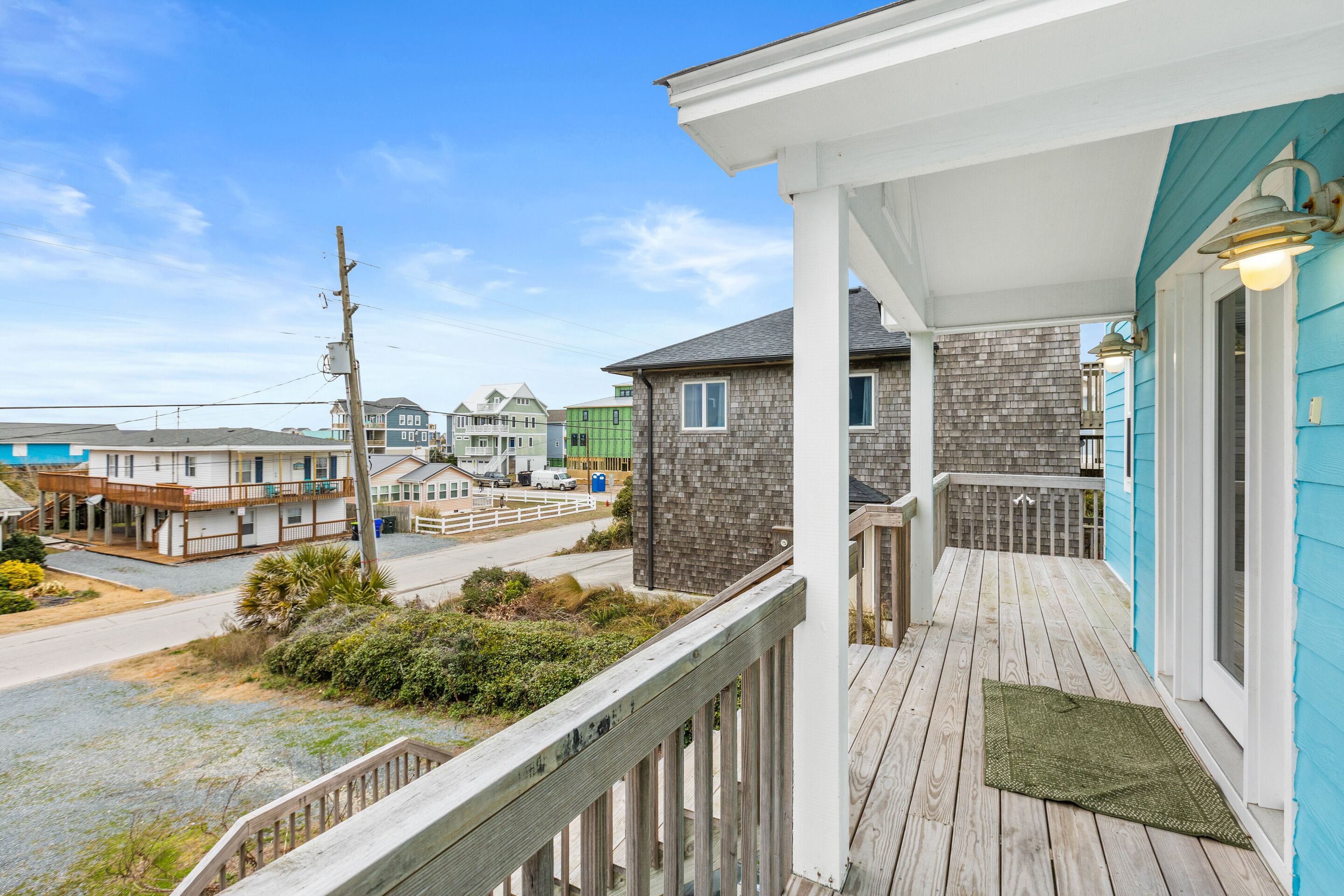 A wooden deck with a white railing, a green doormat, and a view of neighboring houses.