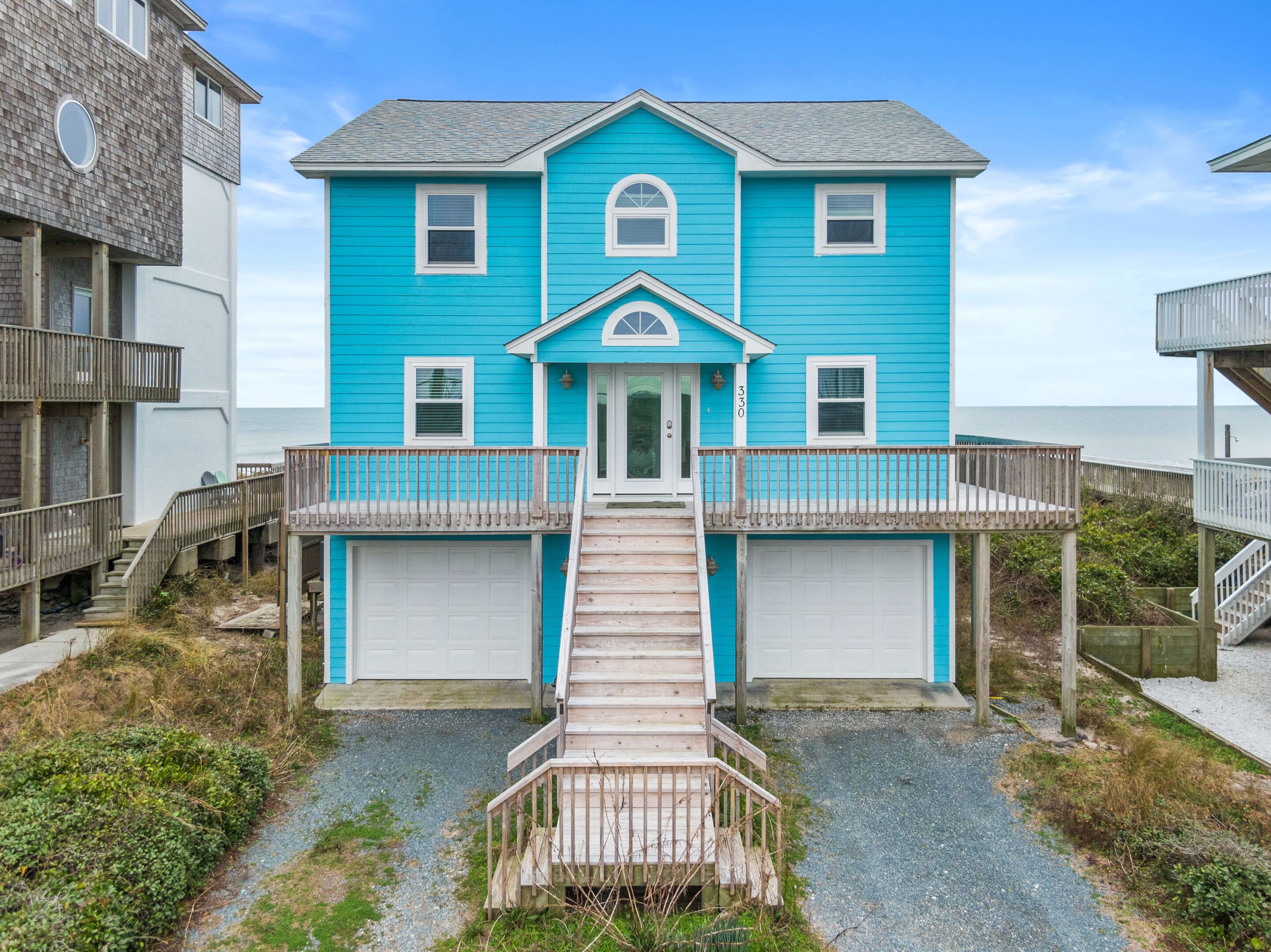 A two-story house with a front porch, a garage, and a wooden staircase leading to the entrance.