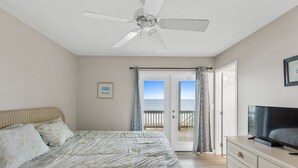 A bedroom with a bed, a television on a dresser, and a ceiling fan. - Renegade by Topsail Realty (Holly Ridge)