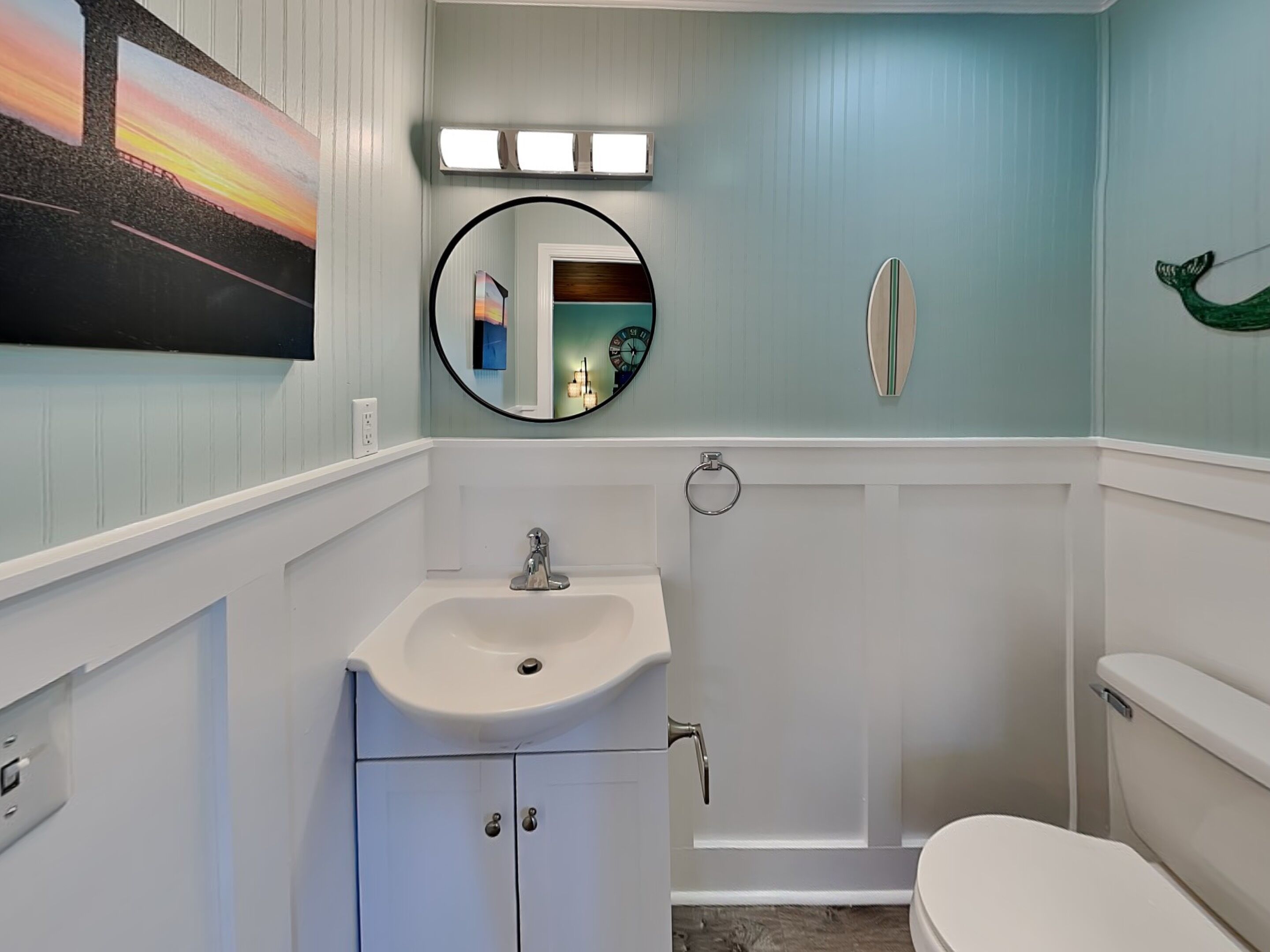 Ein Badezimmer mit Waschbecken, Spiegel, Toilette und einem Bild an der Wand.
