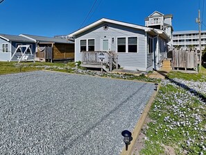 Um bairro residencial com uma casa, um alpendre, um pequeno deque e uma entrada com calçamento de cascalho.