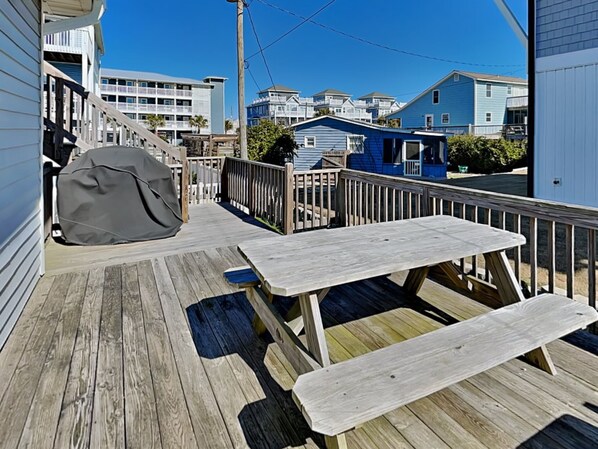 A wooden deck with picnic tables and a covered grill, overlooking a row of blue houses. - Just Sandy by Topsail Realty (Holly Ridge)