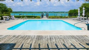 Ein rechteckiger Pool mit Holzterrasse im Vordergrund, einer Metallgeländer und im Hintergrund Meerblick und Grünflächen.