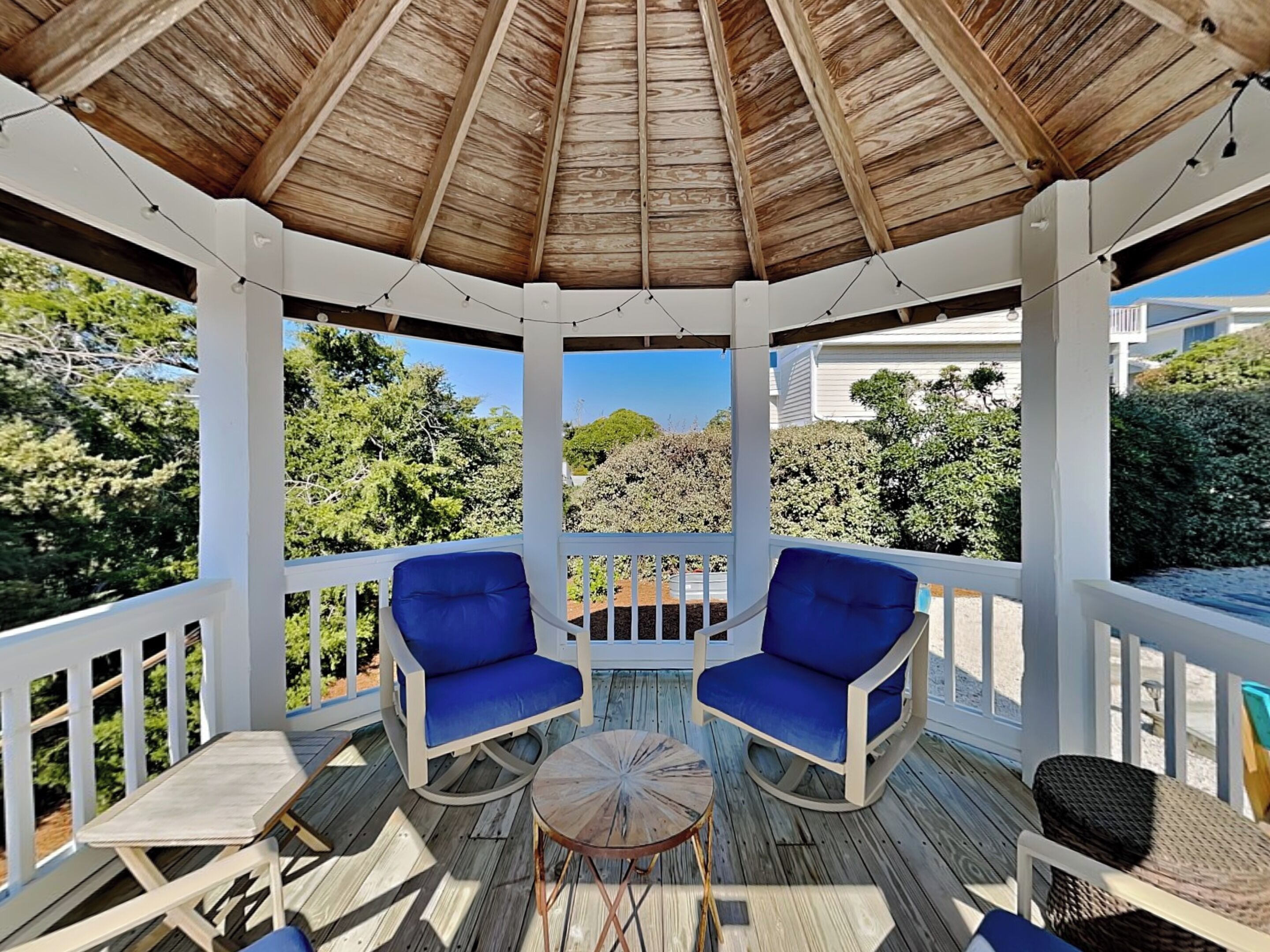 A covered outdoor seating area with two blue cushioned chairs and a small round table.