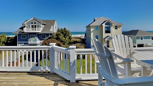 Eine Holzterrasse mit weißen Geländern mit Blick auf einen Strand und Häuser.