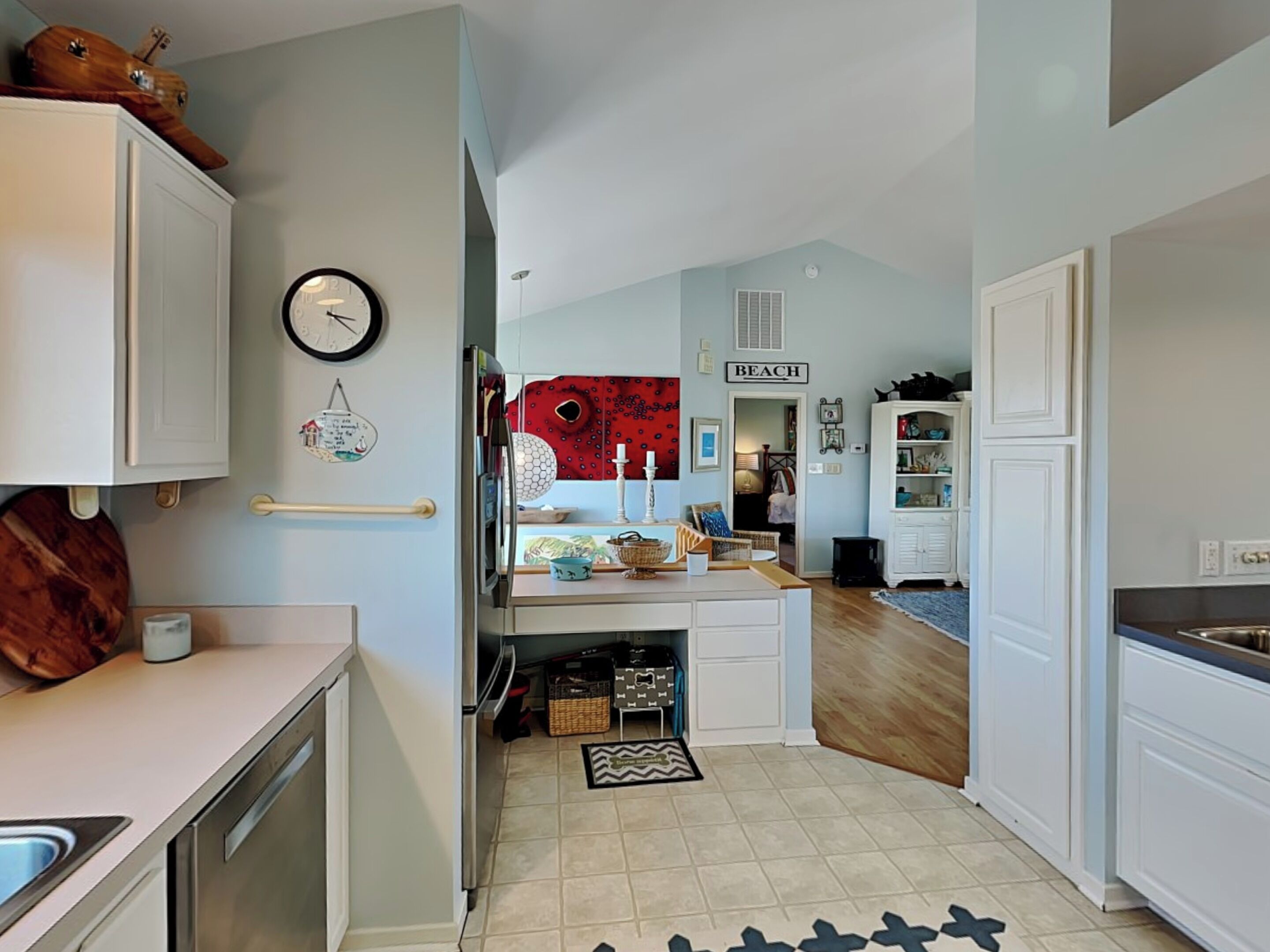 A compact kitchen with a built-in oven, a clock, and a 'BEACH' sign on the wall.