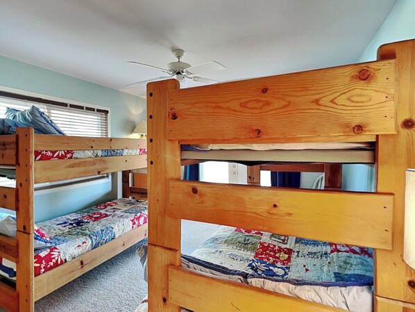 A room with two bunk beds, a ceiling fan, and a window with blinds. - The Shell Collector by Topsail Realty (Holly Ridge)