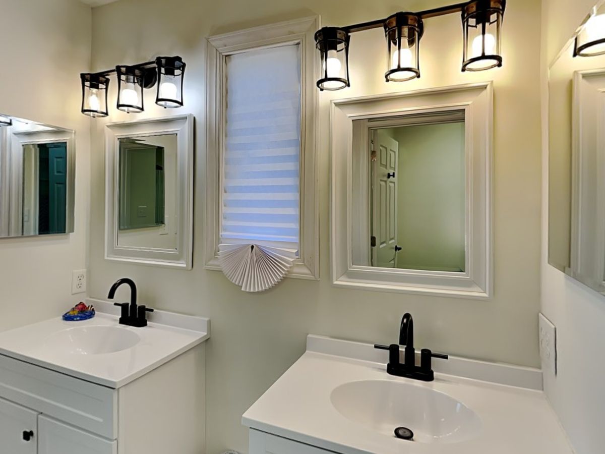 A bathroom with two sinks, a mirror above each sink, and a window with blinds.