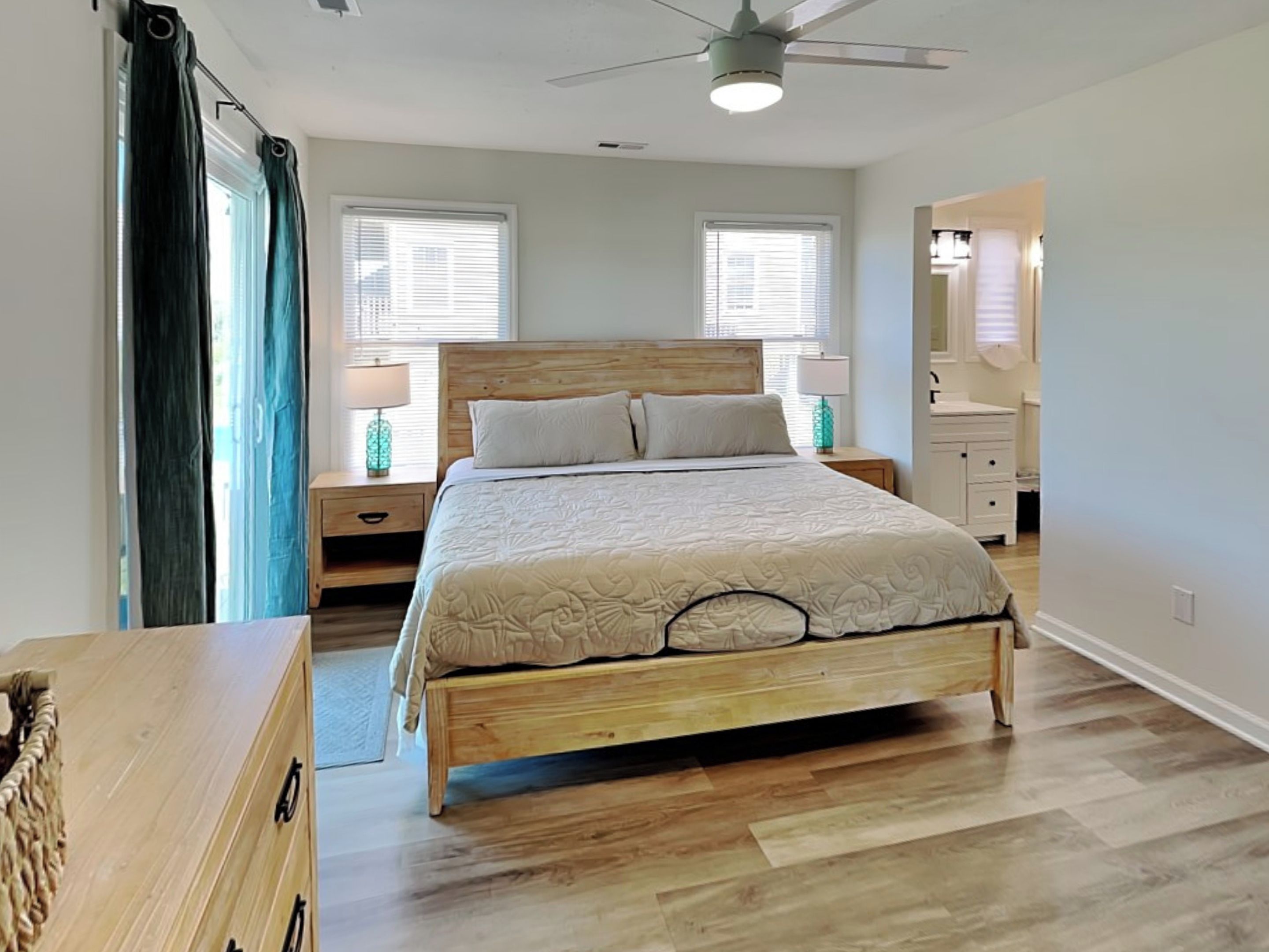 A bedroom with a wooden bed, two bedside tables with lamps, a ceiling fan, and a window with blinds.