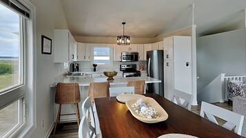 A modern kitchen with white cabinetry, a central island, and a dining area with a wooden table and chairs.