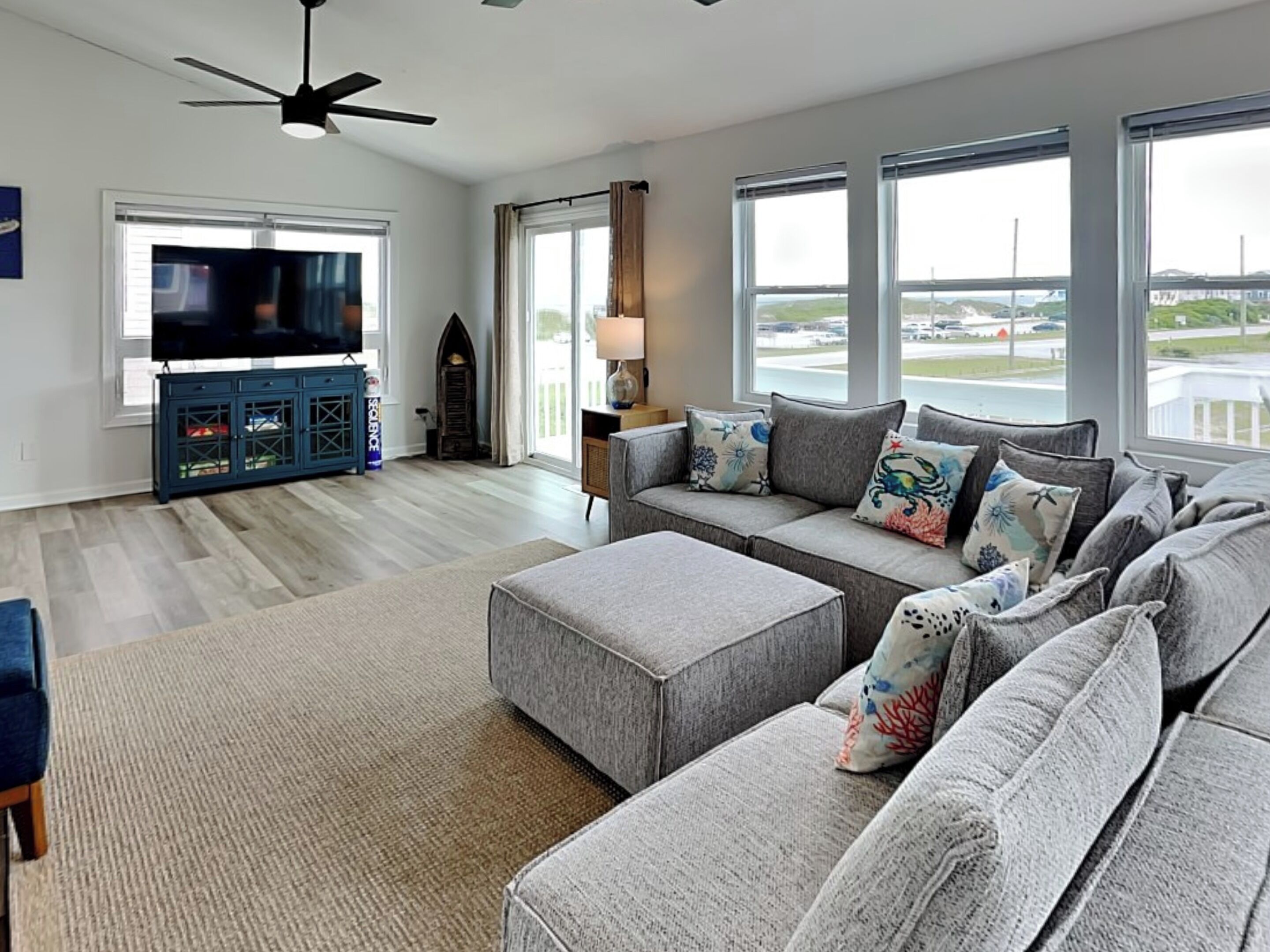 A modern living room with a grey sofa set, a flat-screen TV, and a ceiling fan.