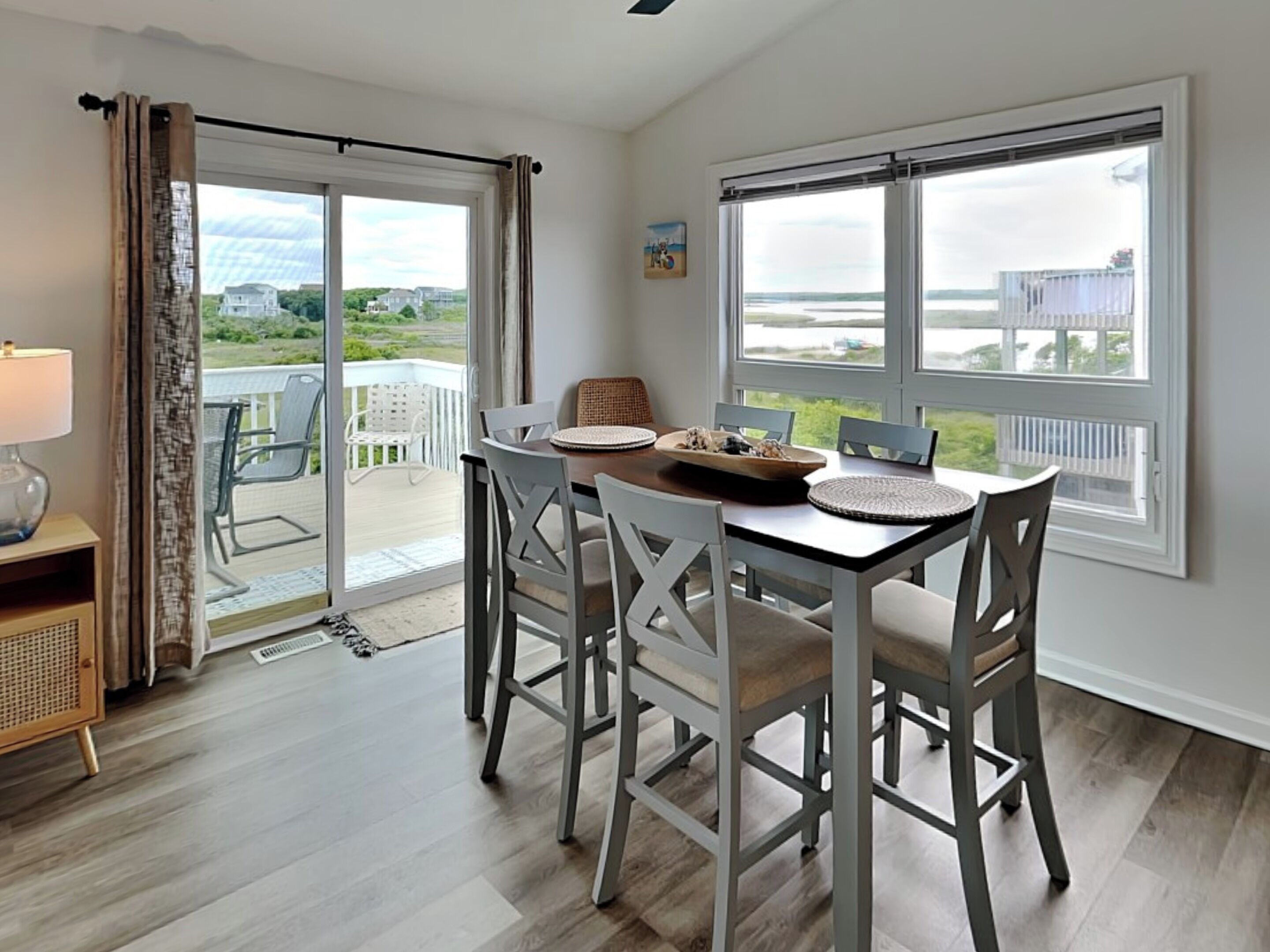 Spiseområde med et bord til fire, store vinduer med havudsigt og en skydedør, der fører til en udendørs terrasse.