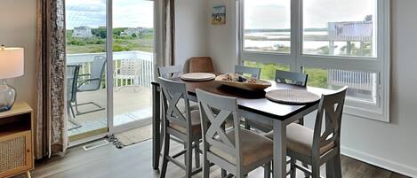 Spiseområde med et bord til fire, store vinduer med havudsigt og en skydedør, der fører til en udendørs terrasse.