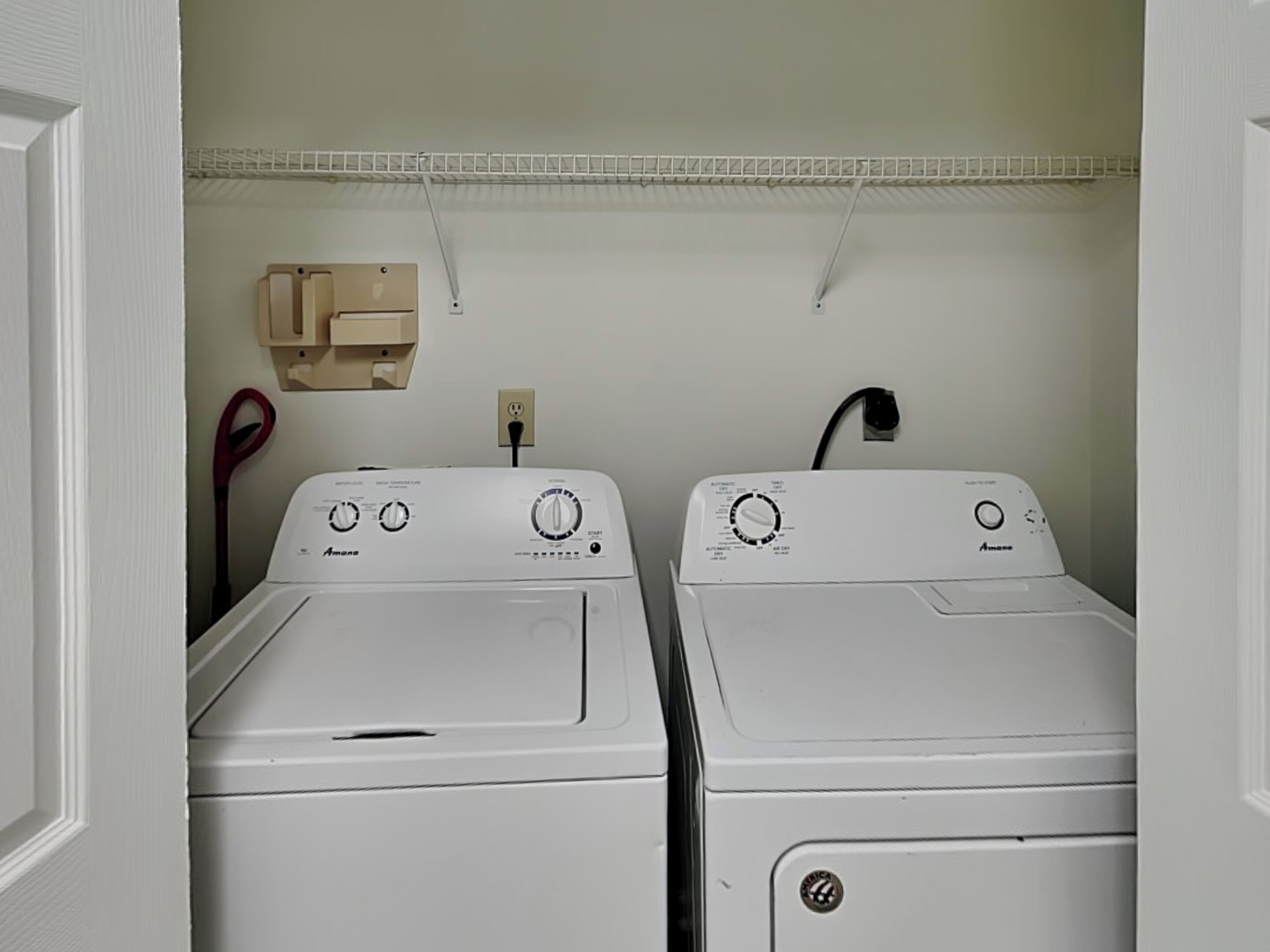 A laundry room with two front-loading Amana washers and dryers, a white wall, and a small wooden cabinet.