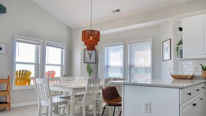 A modern kitchen with white cabinetry, a central island, and a dining area with white chairs and a table. - Sandy By The Sea by Topsail Realty (Sneads Ferry)