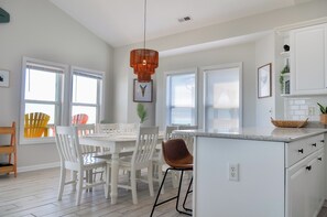 A modern kitchen with white cabinetry, a central island, and a dining area with white chairs and a table. - Sandy By The Sea by Topsail Realty (Sneads Ferry)