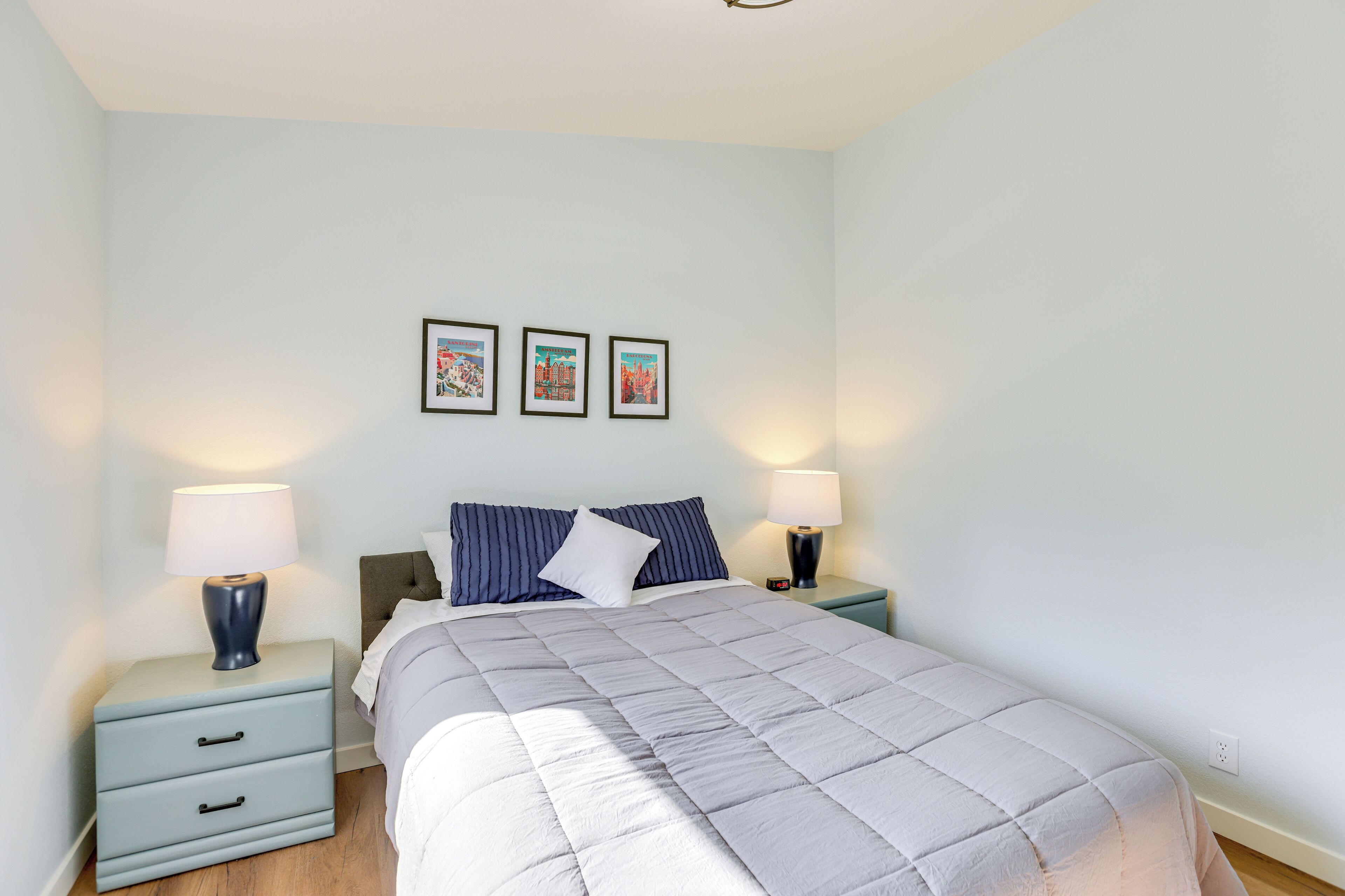 A bedroom with a bed, two bedside tables, a nightstand, and three framed pictures on the wall.
