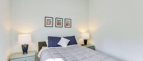 A bedroom with a bed, two bedside tables, a nightstand, and three framed pictures on the wall.